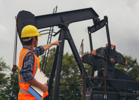 Workers standing and checking beside working oil pumps.