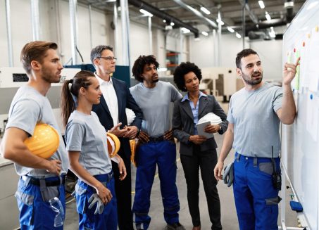 Happy manual worker presenting the results of business development while giving presentation to company leaders and his team in a factory.